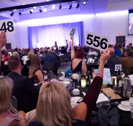 In a large crowd of people, women hold up bidder numbers for an auction.