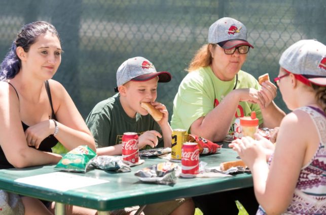 A group of people sit around a sunny picnic table eating lunch.