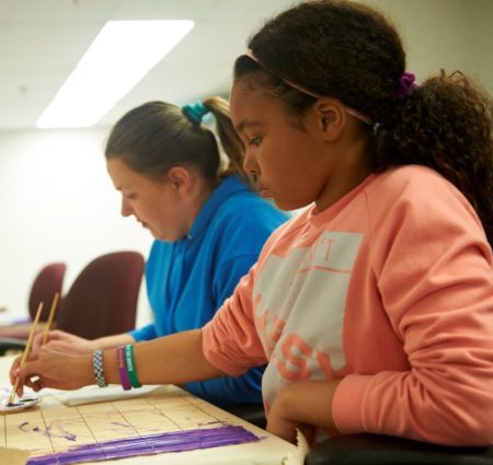 Two people work on individual craft projects at a table.