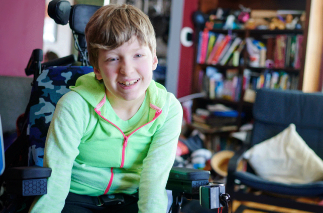 A teenager in bright green leans forward in wheel chair, smiling
