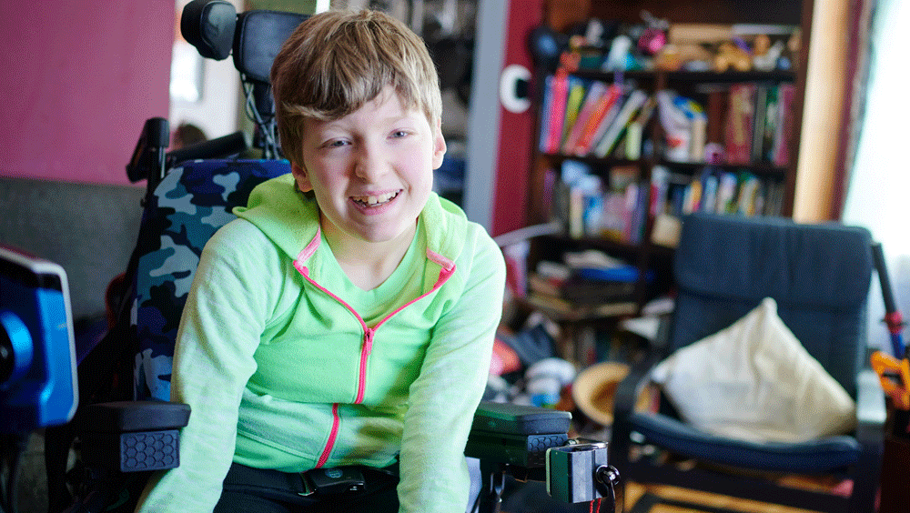 A teenager in bright green leans forward in wheel chair, smiling