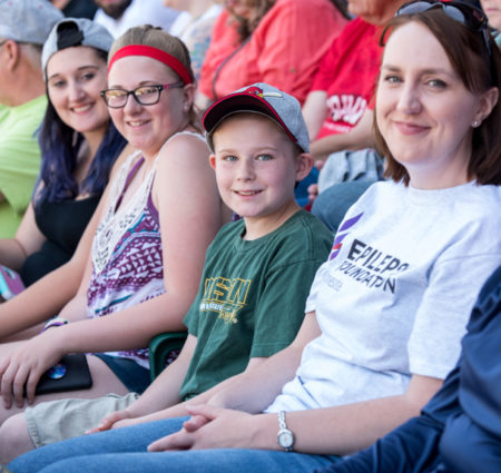 A group of people sit together in a row at a baseball game.