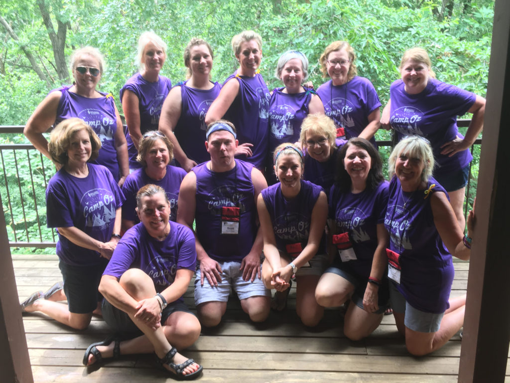 A group of 20 camp counselors and nurses group together on a balcony wearing matching camp oz t-shirts.