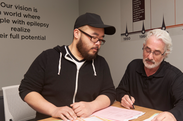 Two men sitting at a table looking at a stack of papers.