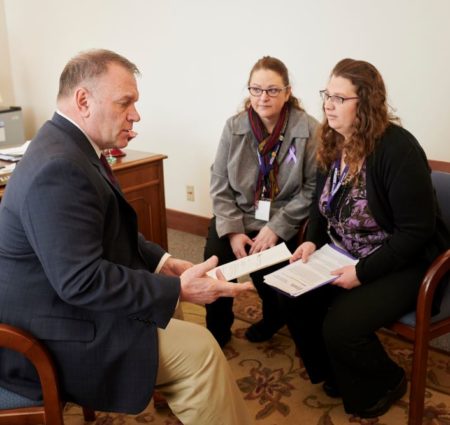 Two women sit and talk with a legislator in his office, each holding pages of information.