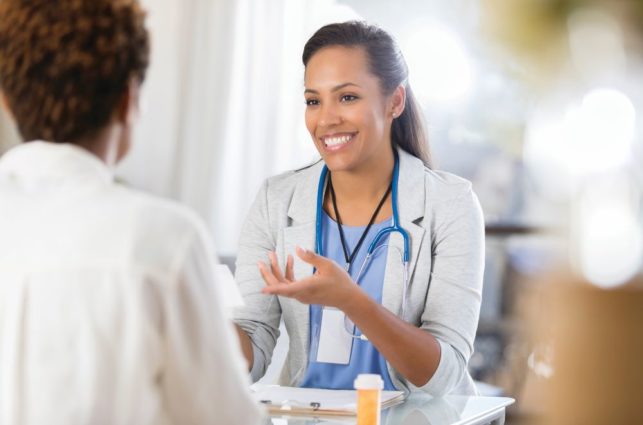 A doctor smiles at her patient and gestures with her hands.