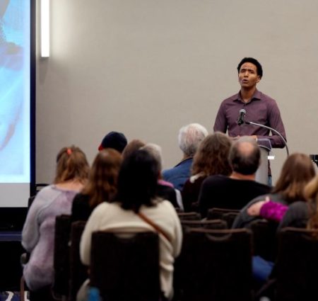 A speaker presents to a crowd in a large conference room.