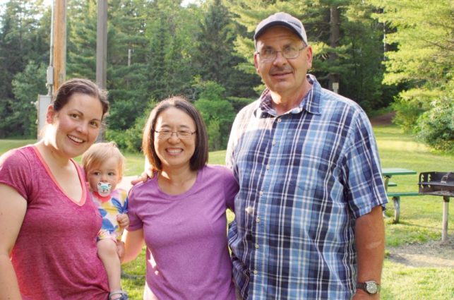 A group of people and a baby smile with their arms around each other.