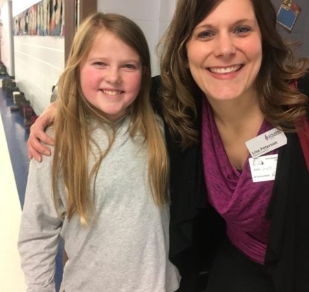 A woman poses with her arm around a child, both smiling.