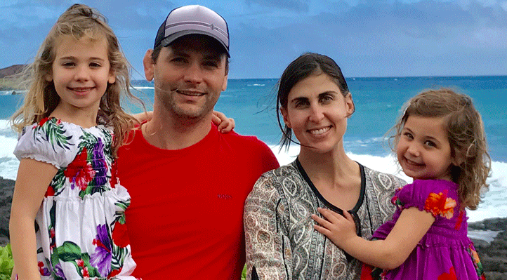 A family with two young children smile for a portrait in front of an ocean view