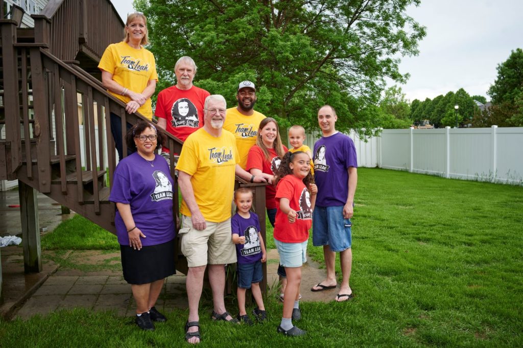 A family wearing brightly colored shirts groups together in their backyard for a team photo
