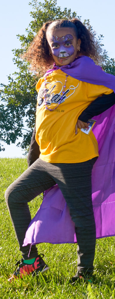 A child in a purple superhero cape and facepaint poses for the camera at the Rise Above Seizures walk