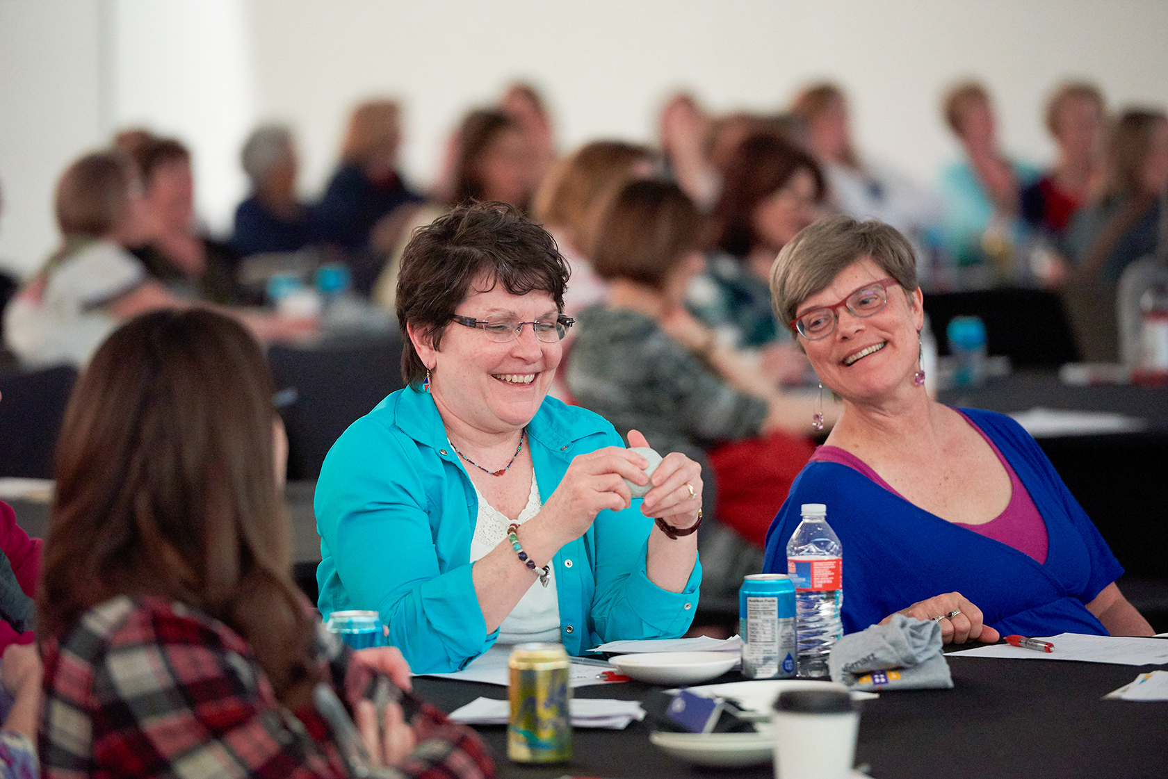 Two adult women at a group training smiling and holding a stress ball brain