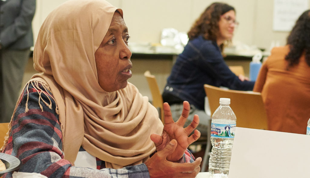 Woman in 60's in hijab talking at table of people