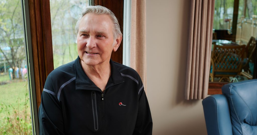 73 year old man smiling out window in home