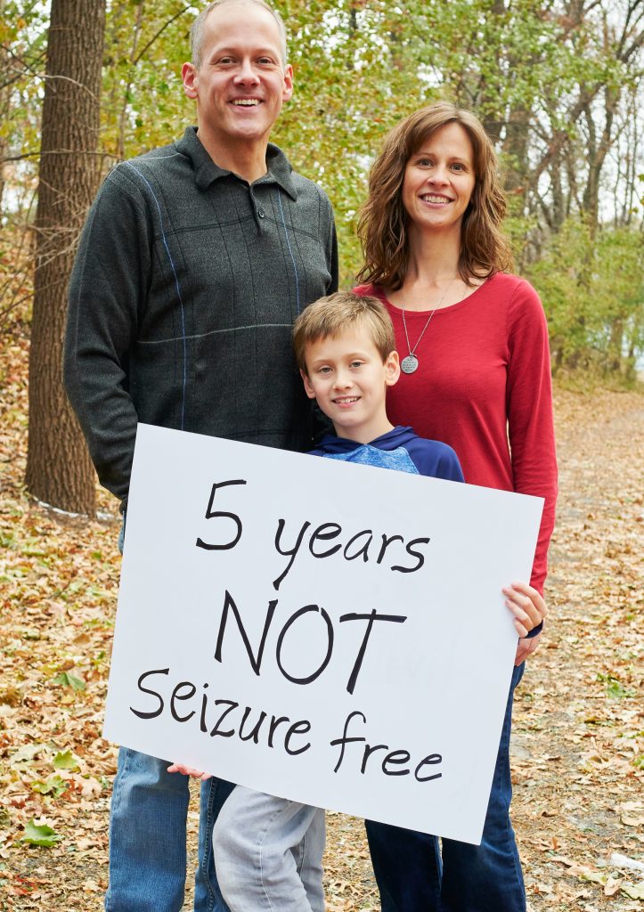 Husband, wife, and son smiling and holding a sign 5 years not seizure free