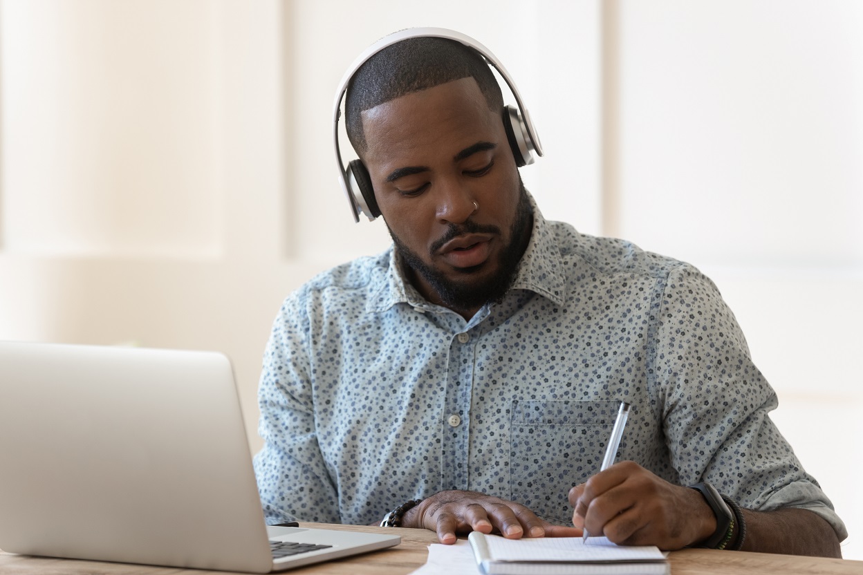 Man at computer with headphones taking notes