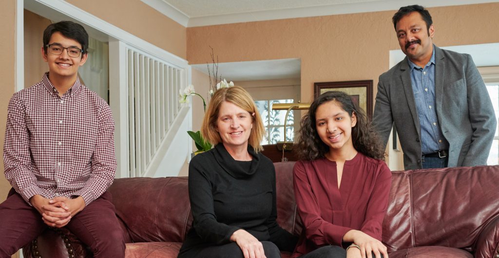 adult male standing, teen male, adult woman, teen woman sitting on couch