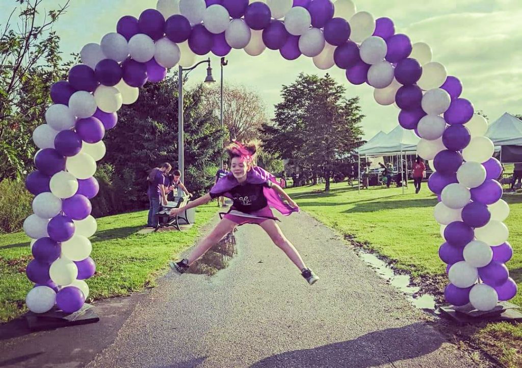 Teenage girl jumping under balloon arch