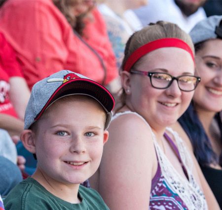 Photo of two people sitting in stadium seats looking at the camera and smiling.