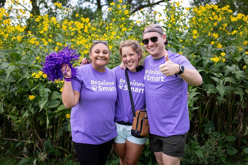 Three EFMN Community members wearing purple shirts with purple pom-pom and giving a thumbs up