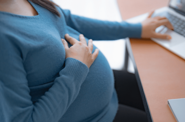 Pregnant person with hand resting on belly researching information on a laptop