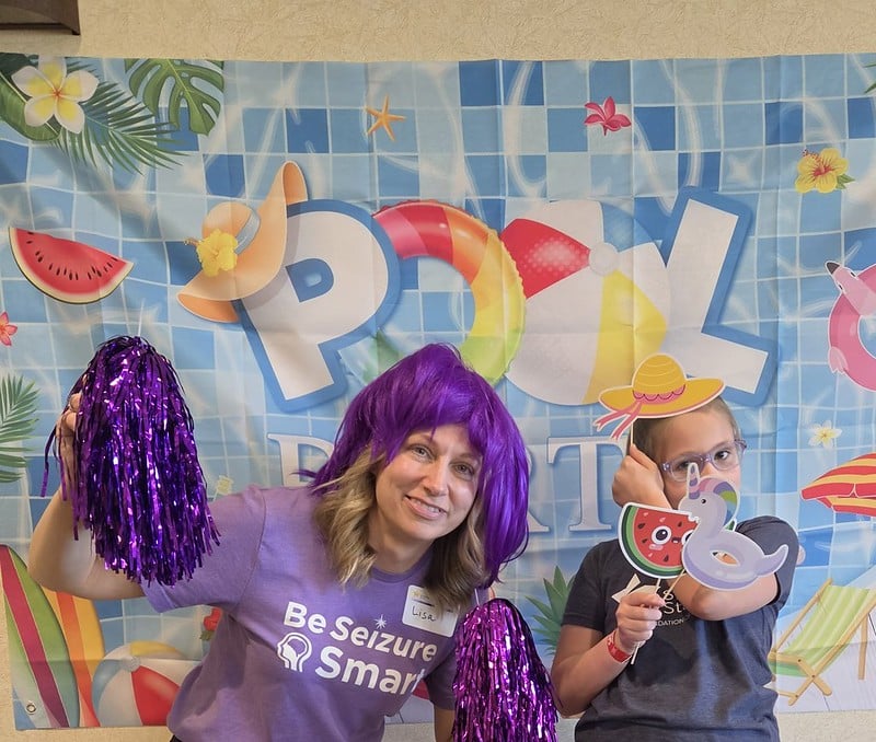 Outreach Manager Lisa N poses for a photo at the photo booth in a purple wig with purple pom poms