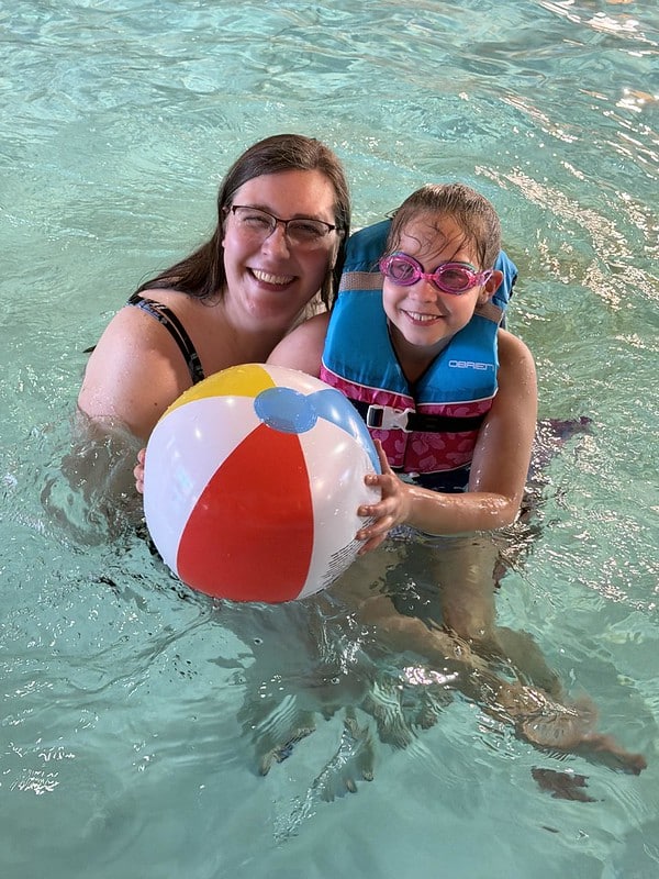 Family with a youth wearing goggles and life vest holding a beach ball while in the pool at the waterpark