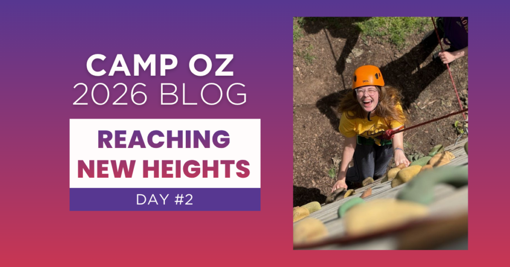 Person wearing an orange helmet climbs a camp rock wall outdoors, looking upward while secured with a rope, next to text reading “Camp Oz 2026 Blog — Reaching New Heights Day #2” on a purple gradient background.