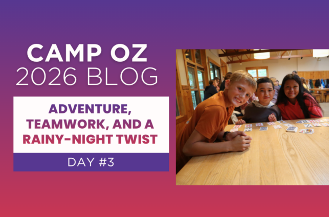 Three campers gathered around a wooden table playing a card game inside a camp lodge, with other campers in the background; graphic text reads “Camp Oz 2026 Blog – Day #3: Adventure, Teamwork, and a Rainy-Night Twist