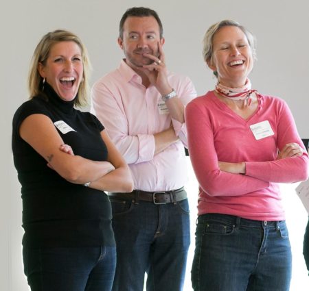 4 people stand with their arms crossed, laughing.